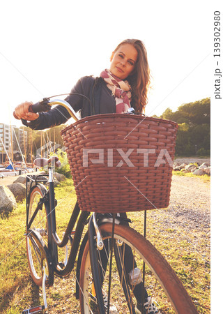 Portrait, flare and a girl with her bicycle in the park for travel, freedom or eco friendly adventure. Summer, cycling and a young person outdoor in the countryside for a cycling ride with a basket 139302980