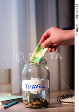 Travel savings in jar. Money being added to travel themed savings container. Inspires adventure planning and purposeful financial habits. Vertical photo Travel savings in jar. Money being added to travel themed savings container. Inspires adventure planning and purposeful financial habits. Vertical photo 139303311