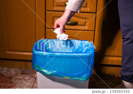 Hand placing used piece of paper into trash bin. Showcases proper waste segregation and environmental responsibility. Responsible recycling in home interior Hand placing used piece of paper into trash bin. Showcases proper waste segregation and environmental responsibility. Responsible recycling in home interior 139303350