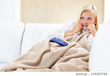 Horror, fear and woman on sofa watching tv with remote, blanket and streaming movies in home. Terror, television and girl on couch in living room with shock for scary video, film or network show. Horror, fear and woman on sofa watching tv with remote, blanket and streaming movies in home. Terror, television and girl on couch in living room with shock for scary video, film or network show. 139303789
