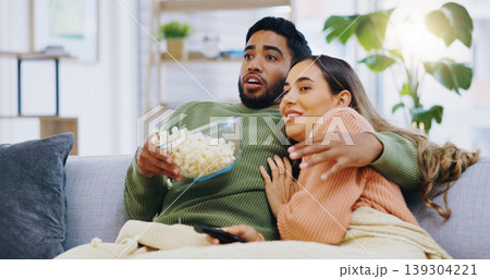 Fear, hug and couple watching tv with popcorn on a sofa for movie, film or streaming show in their home. Wow, television and people embrace in a living room with cinema snack for horror or series Fear, hug and couple watching tv with popcorn on a sofa for movie, film or streaming show in their home. Wow, television and people embrace in a living room with cinema snack for horror or series 139304221