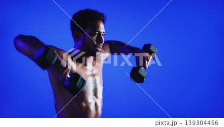 Fitness, weight training or man in studio with dumbbell, power or bicep lift in bodybuilding. Exercise, space or person on blue background with equipment, intense workout or strength in muscle gain. Fitness, weight training or man in studio with dumbbell, power or bicep lift in bodybuilding. Exercise, space or person on blue background with equipment, intense workout or strength in muscle gain. 139304456