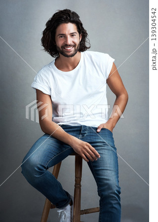 Fashion, smile and portrait of man in studio on a stool with casual, cool and stylish outfit. Happy, handsome and confident young male model from Mexico with trendy style on chair by gray background. Fashion, smile and portrait of man in studio on a stool with casual, cool and stylish outfit. Happy, handsome and confident young male model from Mexico with trendy style on chair by gray background. 139304542
