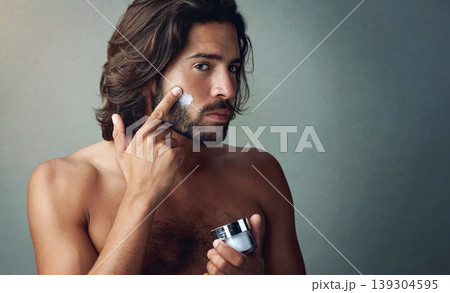 Portrait, skincare or lotion with a shirtless man in studio on a gray background for his grooming routine. Beauty, facial and and the body of a handsome young person with antiaging cream for his skin Portrait, skincare or lotion with a shirtless man in studio on a gray background for his grooming routine. Beauty, facial and and the body of a handsome young person with antiaging cream for his skin 139304595
