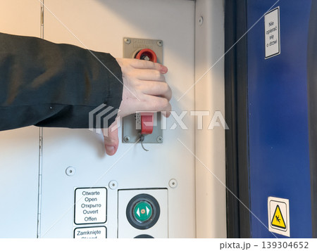 Hand pulling emergency lever on train door control panel, indicating safety and passenger transport system operation Hand pulling emergency lever on train door control panel, indicating safety and passenger transport system operation 139304652