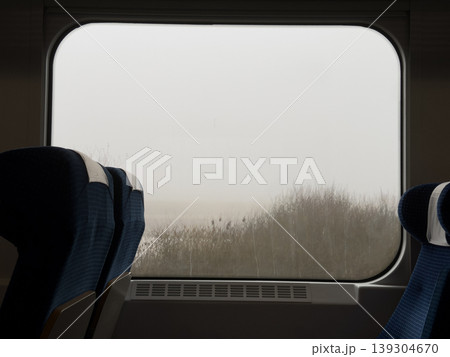 Empty blue fabric train seats face a hazy, muted landscape through a large window, evoking contemplation and journey Empty blue fabric train seats face a hazy, muted landscape through a large window, evoking contemplation and journey 139304670