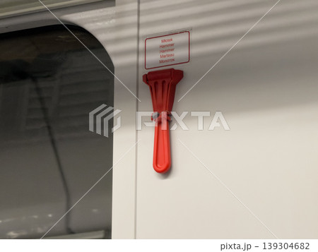 Red safety hammer attached to wall near emergency exit with multilingual text indicating 'Hammer' for immediate use during transport emergencies Red safety hammer attached to wall near emergency exit with multilingual text indicating 'Hammer' for immediate use during transport emergencies 139304682