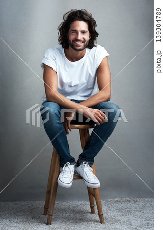 Fashion, smile and portrait of man in studio on a stool with casual, cool and stylish outfit. Happy, handsome and confident young male model from Mexico with trendy style on chair by gray background. Fashion, smile and portrait of man in studio on a stool with casual, cool and stylish outfit. Happy, handsome and confident young male model from Mexico with trendy style on chair by gray background. 139304789