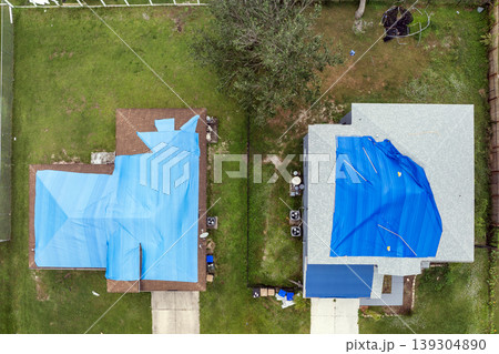 House with hurricane damaged roof, secured by blue tarp to prevent water infiltration until new asphalt shingles can be installed. Temporary protection against rain damage House with hurricane damaged roof, secured by blue tarp to prevent water infiltration until new asphalt shingles can be installed. Temporary protection against rain damage 139304890
