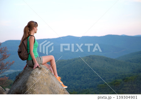 Hiker girl resting on rocky mountain top enjoying summer nature during her travel on wilderness trail. Lonely female traveler traversing high hilltop route. Healthy lifestyle concept Hiker girl resting on rocky mountain top enjoying summer nature during her travel on wilderness trail. Lonely female traveler traversing high hilltop route. Healthy lifestyle concept 139304901