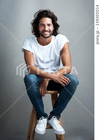 Fashion, smile and portrait of man in studio on a stool with casual, cool and stylish outfit. Happy, handsome and confident young male model from Mexico with trendy style on chair by gray background. 139305014