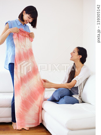 Woman, friend and showing of dress in home for opinion, decision and choice of clothes. Happy people, smiling and excitement for gift with cool, trendy or casual fashion for summer in living room 139305142