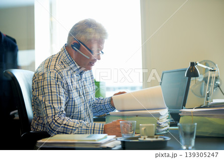 Senior businessman, documents and headphones in call center for communication or online advice at office. Mature man, consultant or agent reading paperwork for legal assistance or help at workplace 139305247