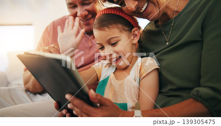 Tablet, video call and child with grandparents on sofa in the living room of modern family house. Happy, virtual communication and girl on digital technology relaxing with senior people at home. Tablet, video call and child with grandparents on sofa in the living room of modern family house. Happy, virtual communication and girl on digital technology relaxing with senior people at home. 139305475