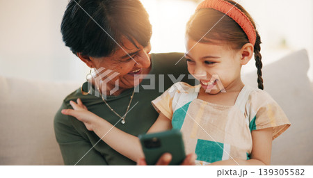 Child, grandmother and cellphone laugh on sofa or online connection, games or bonding. Kid, old woman and smile for social media or funny joke embrace on couch together relax, love or trust safety 139305582