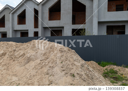 Construction workers prepare sand on the site while close to new buildings. The area shows dirt and building materials with a fence Construction workers prepare sand on the site while close to new buildings. The area shows dirt and building materials with a fence 139308837