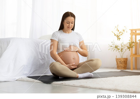 Young pregnant caucasian woman sitting on yoga mat and touching belly Young pregnant caucasian woman sitting on yoga mat and touching belly 139308844
