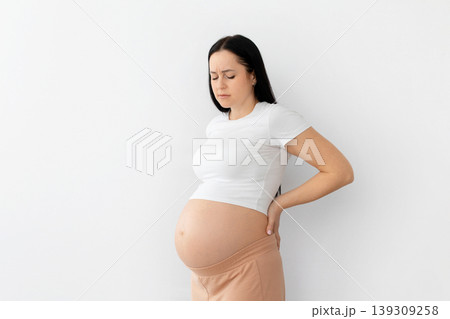 Pregnant young woman holding lower back in discomfort, representing pregnancy pain Pregnant young woman holding lower back in discomfort, representing pregnancy pain 139309258