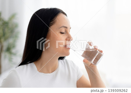Closeup portrait of young woman drinking glass of water with eyes closed Closeup portrait of young woman drinking glass of water with eyes closed 139309262