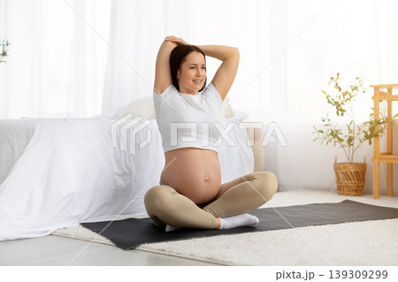 Active pregnant woman sitting on yoga mat stretching arms overhead with smile 139309299