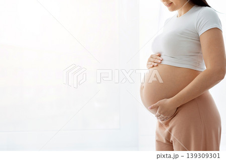 Closeup side profile of pregnant woman holding bare belly with both hands 139309301