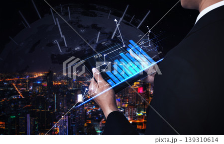 Business professional analyzing futuristic data visualization while overlooking a city skyline at night with glowing graphs and charts on a digital tablet Scalp 139310614