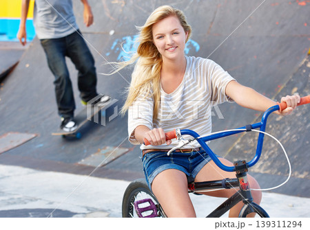 Ride, bike and portrait of teenager at skatepark in summer with friends on vacation or holiday with adventure. Girl, relax and enjoy exercise on bicycle with a smile for sports, event or fun in city 139311294