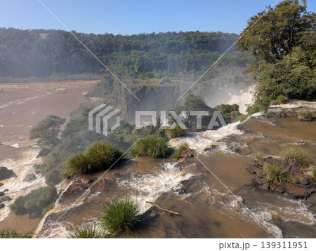 Aerial view of rocks, vegetation, and the turbulent river and Iguazu Falls in Iguazu National Park and Reserve in Argentina in June. Aerial view of rocks, vegetation, and the turbulent river and Iguazu Falls in Iguazu National Park and Reserve in Argentina in June. 139311951
