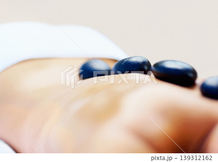 Back, stone massage and person at spa for wellness, holistic therapy or relax in studio on brown background. Beauty salon, skincare and closeup of client with detox rocks for healing muscle treatment Back, stone massage and person at spa for wellness, holistic therapy or relax in studio on brown background. Beauty salon, skincare and closeup of client with detox rocks for healing muscle treatment 139312162