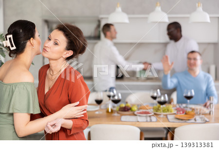 Hospitable hostess warmly greeting and kissing female friend Hospitable hostess warmly greeting and kissing female friend 139313381