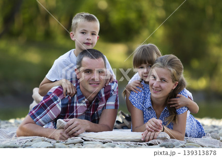Family portrait of young happy mother, father and two cute blond children, boy and girl on bright summer day with green bokeh background. Happy family relations, love, care and perfect holiday concept 139313878