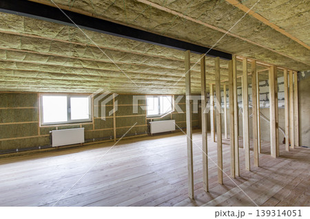 Construction and renovation of big light spacious empty room with oak floor, walls and ceiling insulated with rock wool, heating radiators under low attic windows and wooden frame for future walls. Construction and renovation of big light spacious empty room with oak floor, walls and ceiling insulated with rock wool, heating radiators under low attic windows and wooden frame for future walls. 139314051