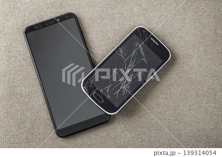 Comparison of two black mobile phones, old cellphone with cracked screen and new modern on light cloth copy space background. Technology progress and replacement concept. 139314054