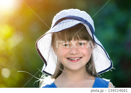 Close-up portrait of happy smiling little girl in a big hat. Child having fun time outdoors in summer. Close-up portrait of happy smiling little girl in a big hat. Child having fun time outdoors in summer. 139314081
