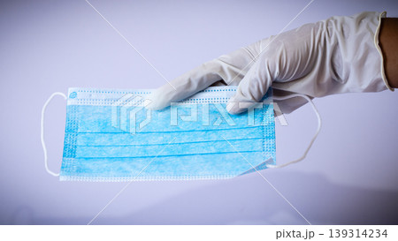 Medical face mask holding in gloved single hand 139314234