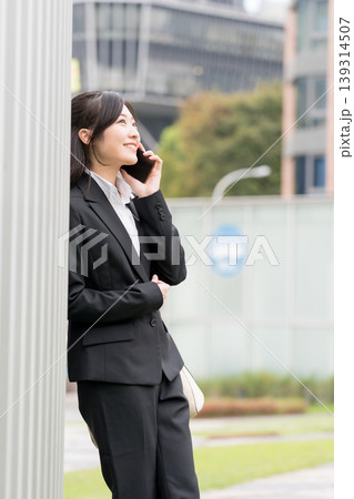 ビジネス街でスマートフォン通話するスーツ姿の女性・就活や仕事イメージ ビジネス街でスマートフォン通話するスーツ姿の女性・就活や仕事イメージ 139314507