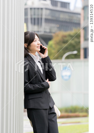 ビジネス街でスマートフォン通話するスーツ姿の女性・就活や仕事イメージ ビジネス街でスマートフォン通話するスーツ姿の女性・就活や仕事イメージ 139314510