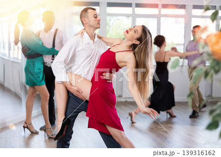 Elegant duet of a man and a woman in festive dresses dances a passionate tango during a group dance lesson in choreographic studio 139316162