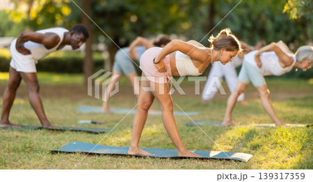 Girl performing Pyramid Pose during group young class in park 139317359