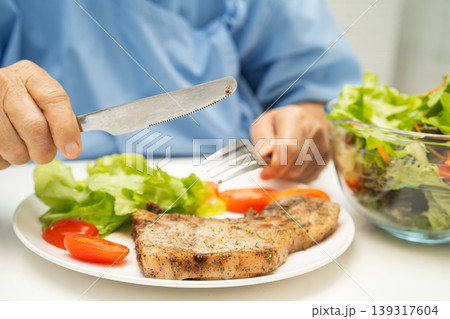 Asian elderly woman patient eating salmon stake and vegetable salad for healthy food in hospital. Asian elderly woman patient eating salmon stake and vegetable salad for healthy food in hospital. 139317604