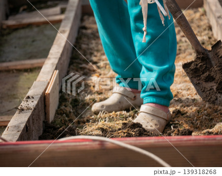 Gardener digging soil in wooden garden bed. Woman planting seed and vegetables in backyard garden. Rural hobby and home gardening lifestyle. Sustainable agriculture and food production work. Gardener digging soil in wooden garden bed. Woman planting seed and vegetables in backyard garden. Rural hobby and home gardening lifestyle. Sustainable agriculture and food production work. 139318268