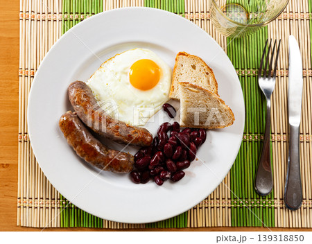Portion of breakfast food is fried egg and pork sausage with stewed beans 139318850