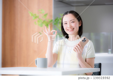 スマートフォンを持ってオッケーポーズの主婦のようなエプロンを着た女性 スマートフォンを持ってオッケーポーズの主婦のようなエプロンを着た女性 139319392