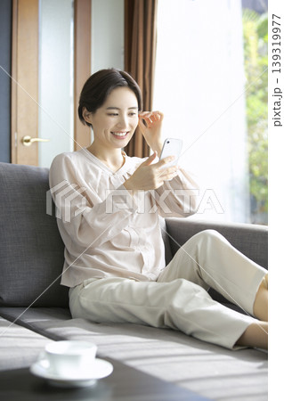 ソファでくつろぎながらスマートフォンを使う女性 休日のリラックスタイム 139319977