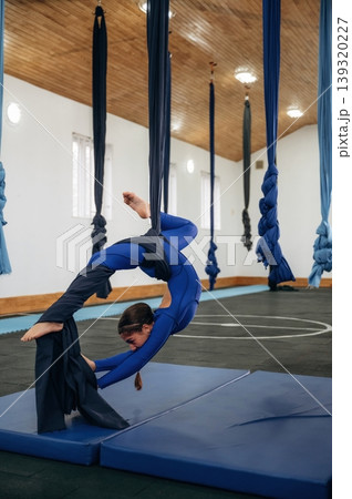 Hanging upside down. Child practicing aerial yoga on hammock straps in a fitness studio Hanging upside down. Child practicing aerial yoga on hammock straps in a fitness studio 139320227