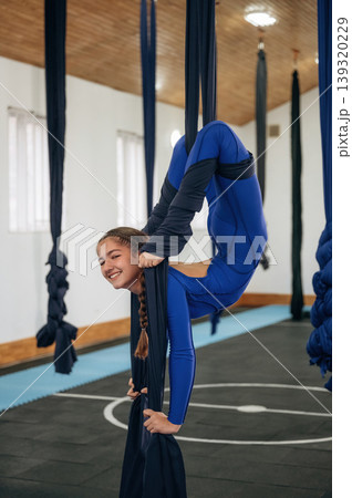 In blue sportive clothes. Child practicing aerial yoga on hammock straps in a fitness studio In blue sportive clothes. Child practicing aerial yoga on hammock straps in a fitness studio 139320229