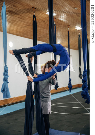 Black color hammock straps. Male instructor assisting a child in aerial yoga practice in a fitness studio 139320281