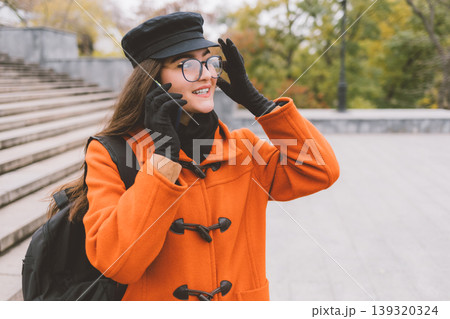 Smiling woman in orange coat talks on phone outdoors Smiling woman in orange coat talks on phone outdoors 139320324