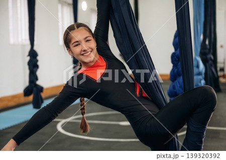 Smiling, having fun. Child practicing aerial yoga on hammock straps in a fitness studio Smiling, having fun. Child practicing aerial yoga on hammock straps in a fitness studio 139320392