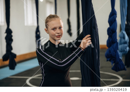 Black clothes, flexibility conception. Child practicing aerial yoga on hammock straps in a fitness studio Black clothes, flexibility conception. Child practicing aerial yoga on hammock straps in a fitness studio 139320419